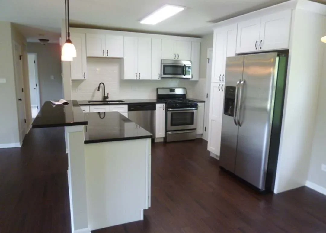 Modern kitchen with white cabinets, black counters, stainless steel appliances, and dark wood flooring