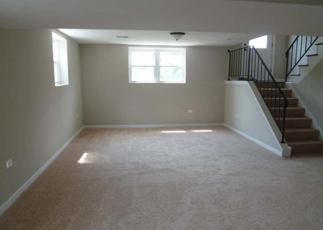 Restored interior room with new carpet, painted walls, windows, and wooden staircase with metal railing