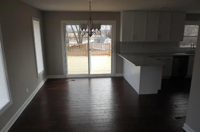 Restored kitchen and dining room with dark hardwood floors, white island, and glass patio doors