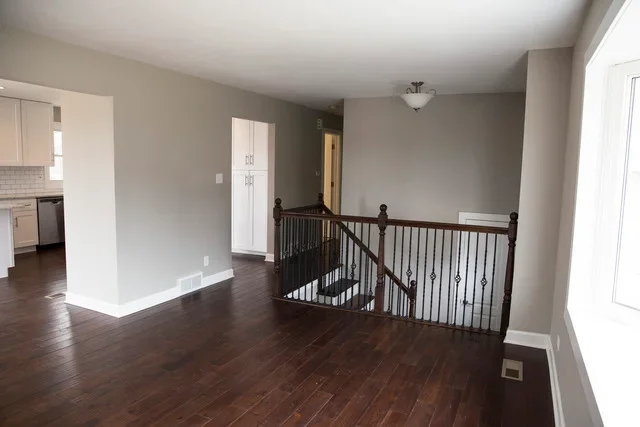 Restored interior with dark hardwood floors, white walls, and black stair railing