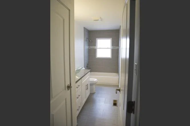 Renovated bathroom with subway tile shower, white vanity, and dark tile flooring
