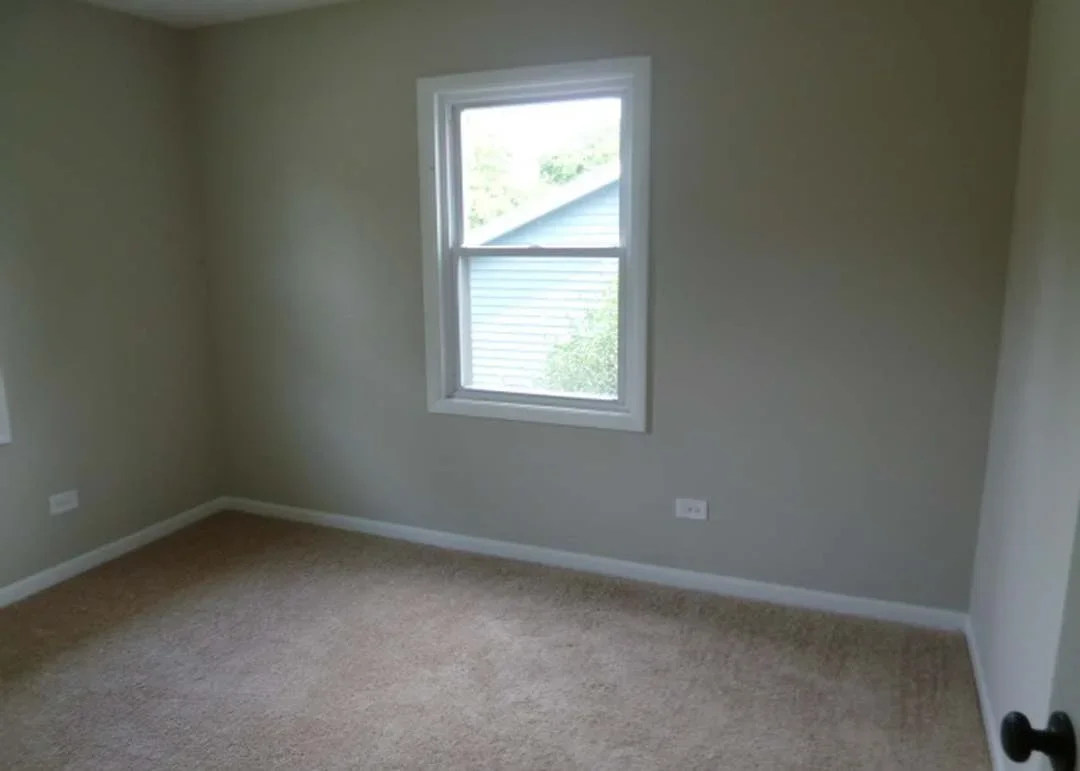 Newly renovated bedroom with white-trimmed window, finished drywall, and new carpet flooring