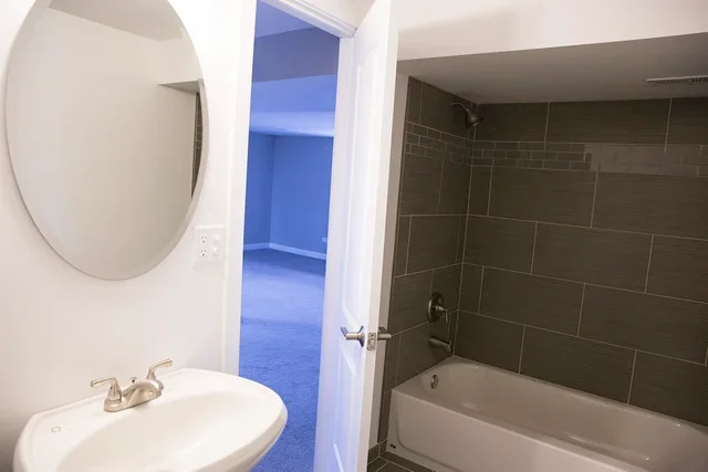 Restored bathroom with dark tile shower, white sink, and round mirror