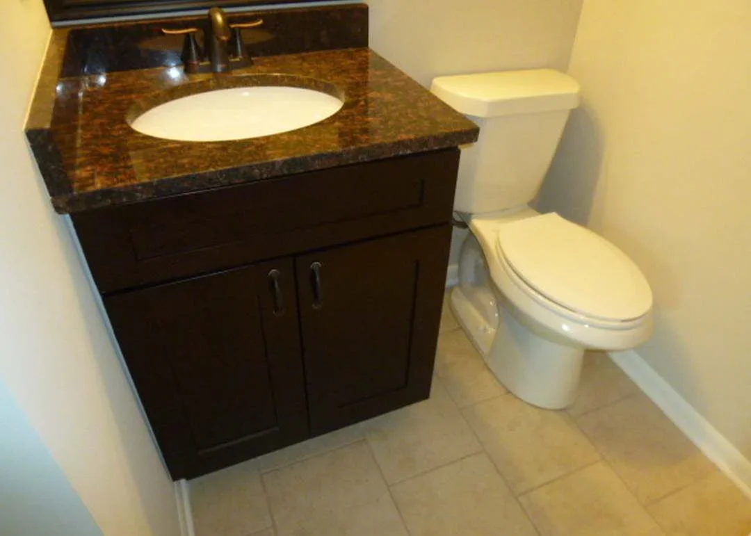 Dark wood bathroom vanity with granite top, white sink, and white toilet in renovated bathroom