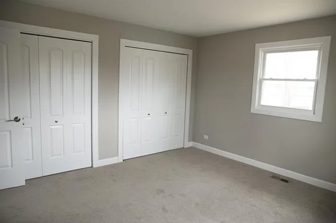 Restored bedroom with taupe walls, new carpet, white closet doors, and window
