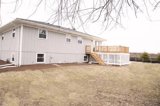 Two-story white metal-sided home with new wooden deck and lattice skirting