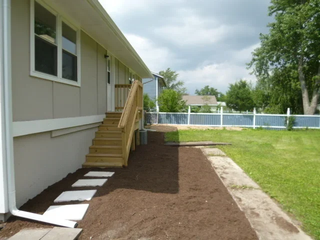New wooden deck with stairs and mulched landscaping bed beside residential home