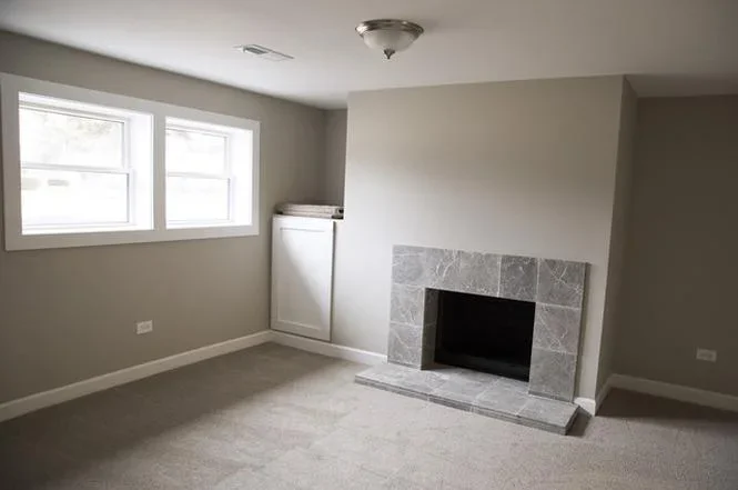 Restored living room with new drywall, neutral paint, tile fireplace, and updated kitchen