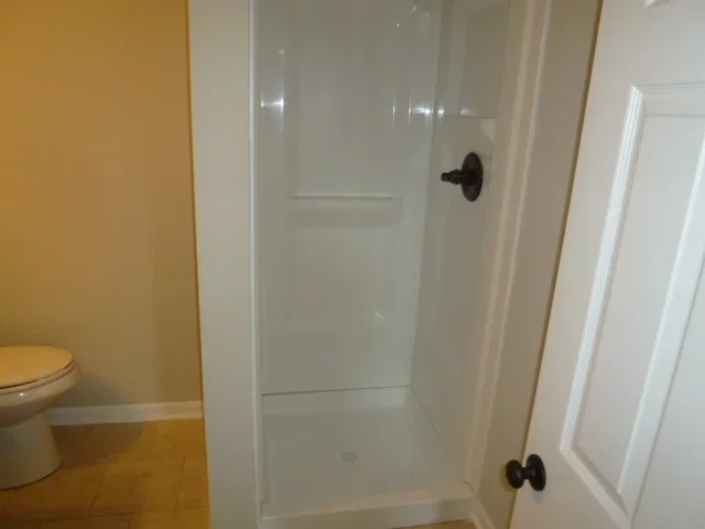 Newly installed white fiberglass shower enclosure with glass doors in restored bathroom