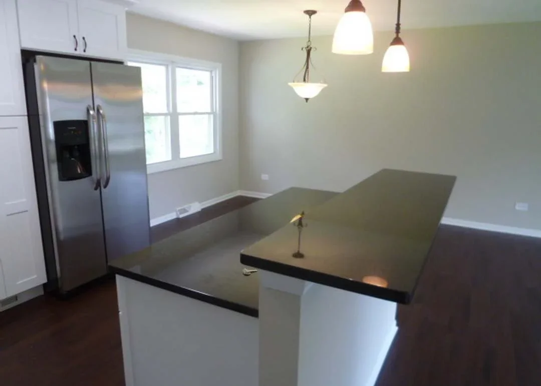 Modern kitchen with white cabinets, stainless steel refrigerator, and dark island countertop