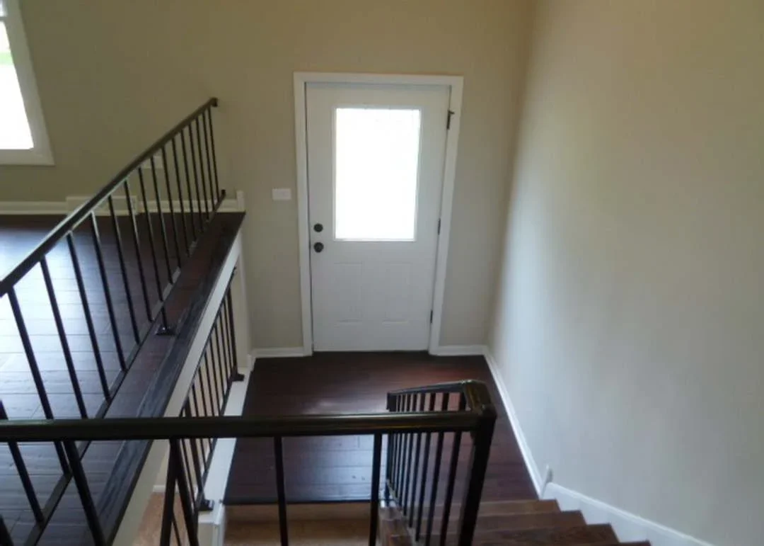 Renovated stairwell with metal railing, white walls, and new entry door