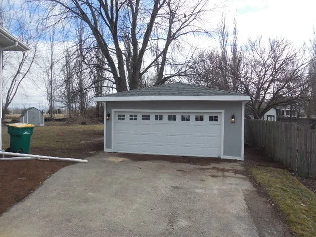 New gray residential garage with white garage door and concrete driveway