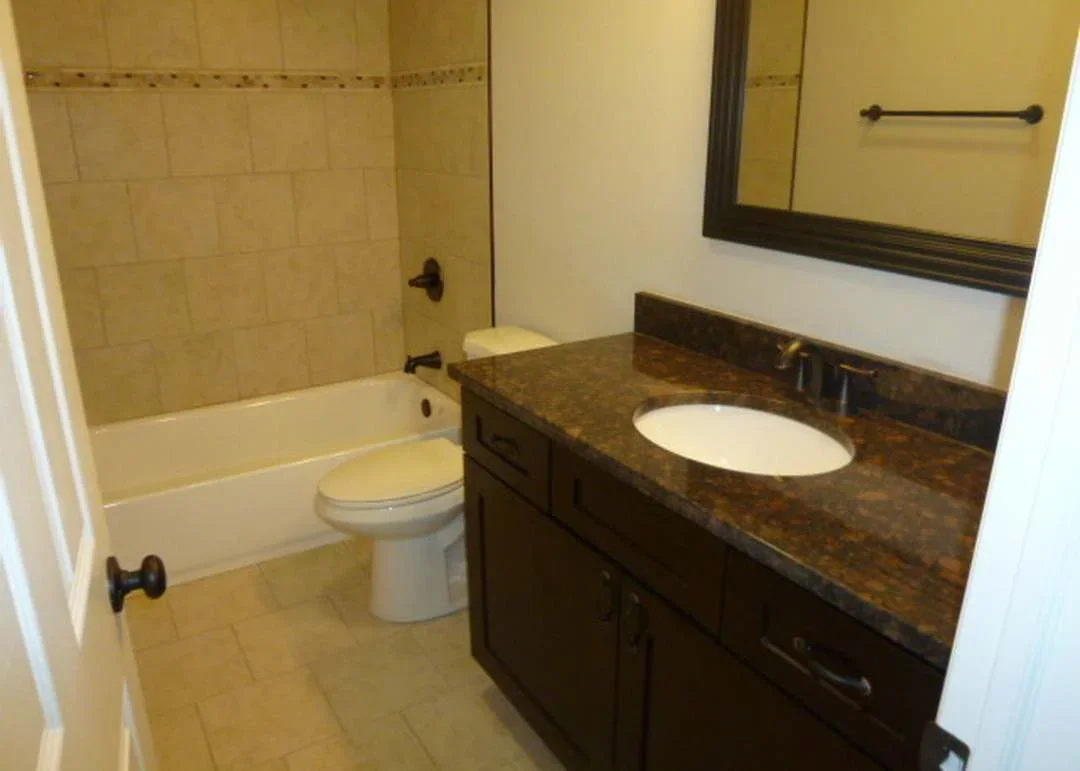 Renovated bathroom with dark vanity, granite countertop, and tiled shower surround