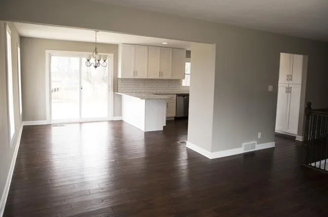 Modern kitchen and living room with white cabinets, dark wood floors, and gray walls